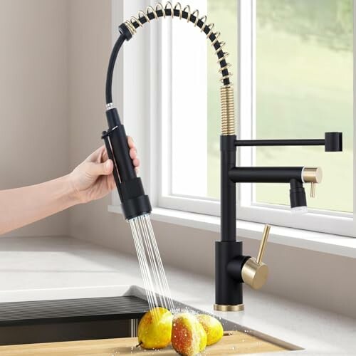 Hand using a black kitchen faucet spraying water on apples.